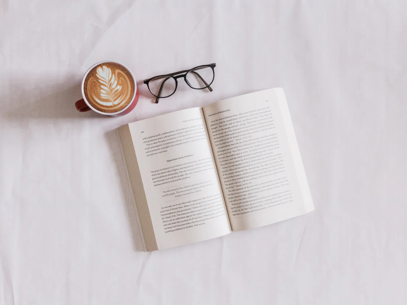 An open book beside a coffee cup and glasses