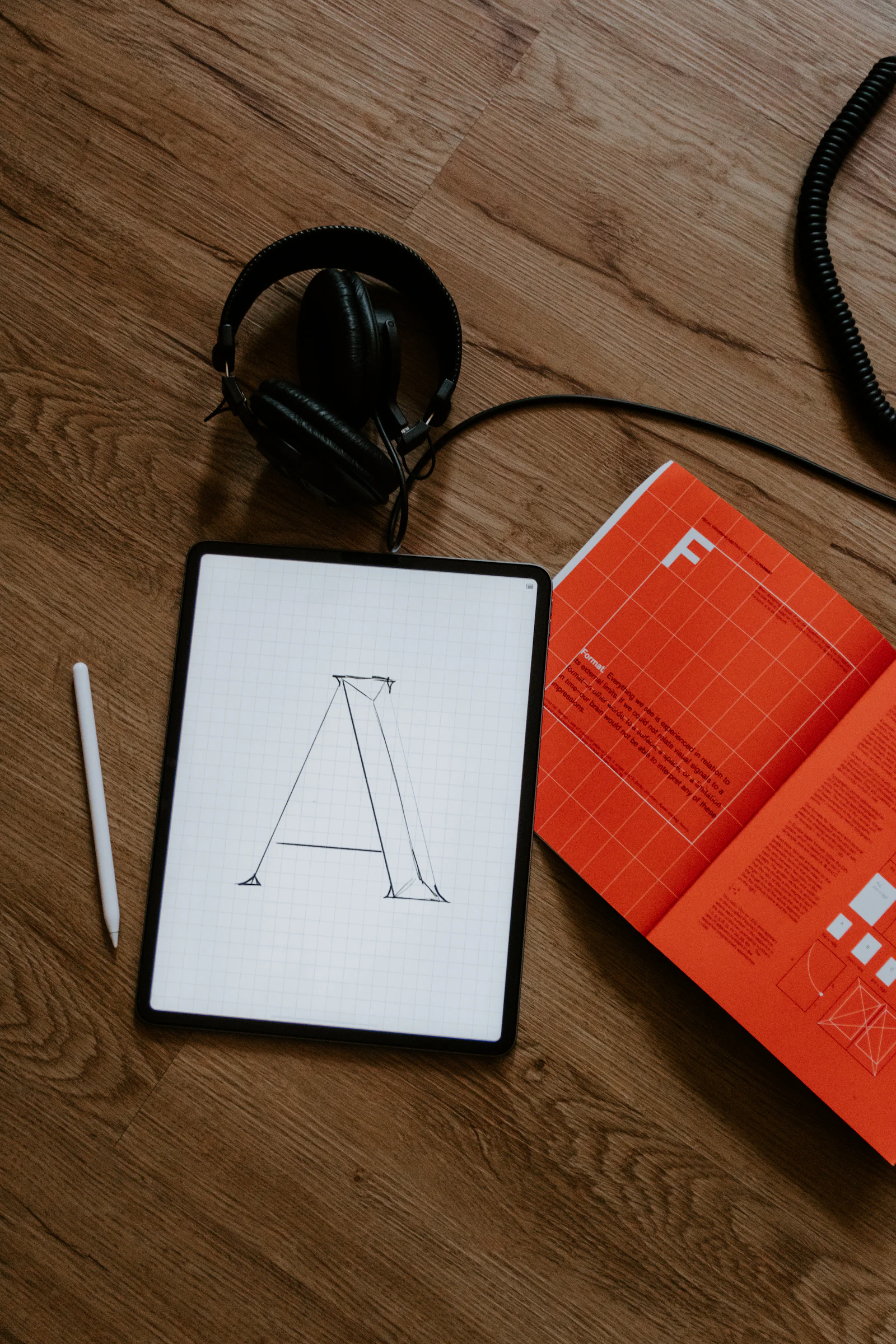 Tablet showing a letterform design beside a printed booklet