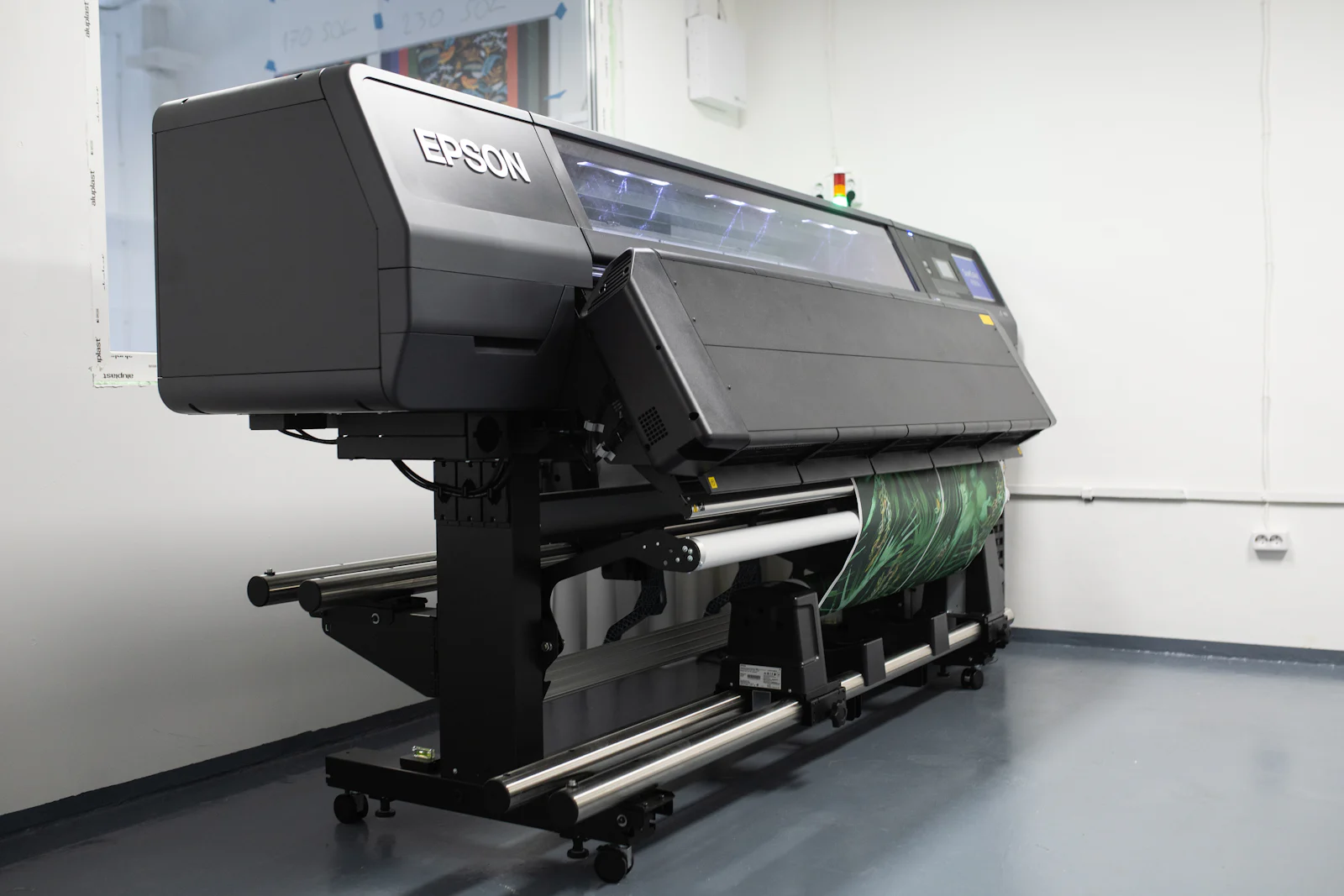 A modern wide-format printer with a printed roll feeding through